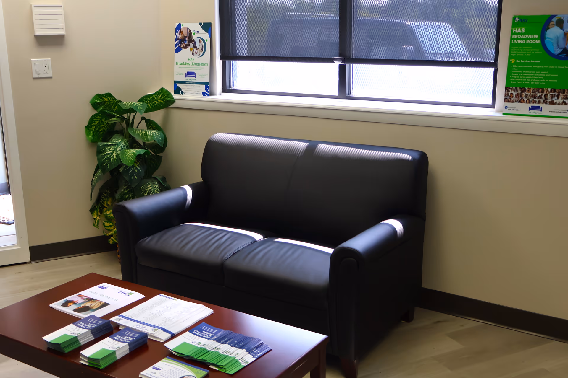 Small lobby seating area with black leather loveseat, plant, and brochures on a coffee table.