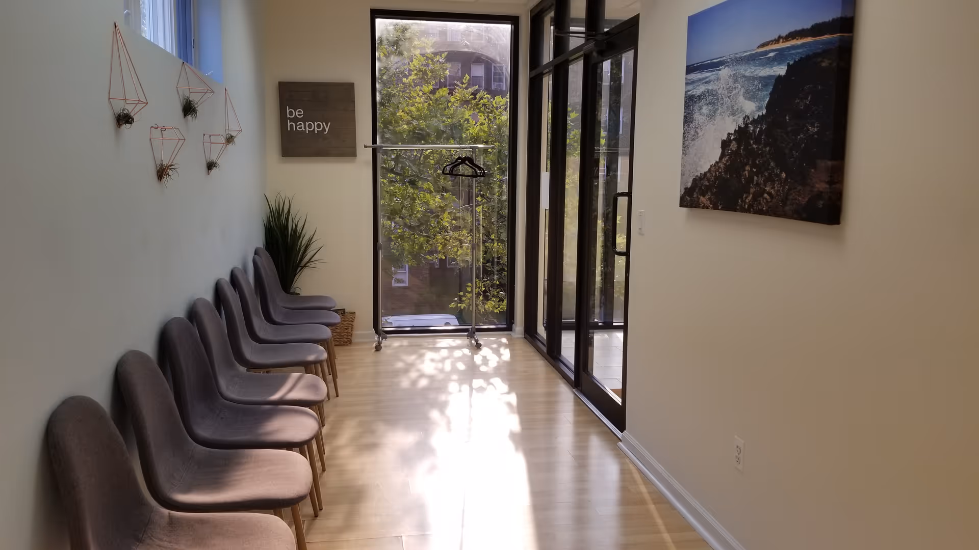 Bright hallway with row of gray chairs along left wall and glass doors at end.
