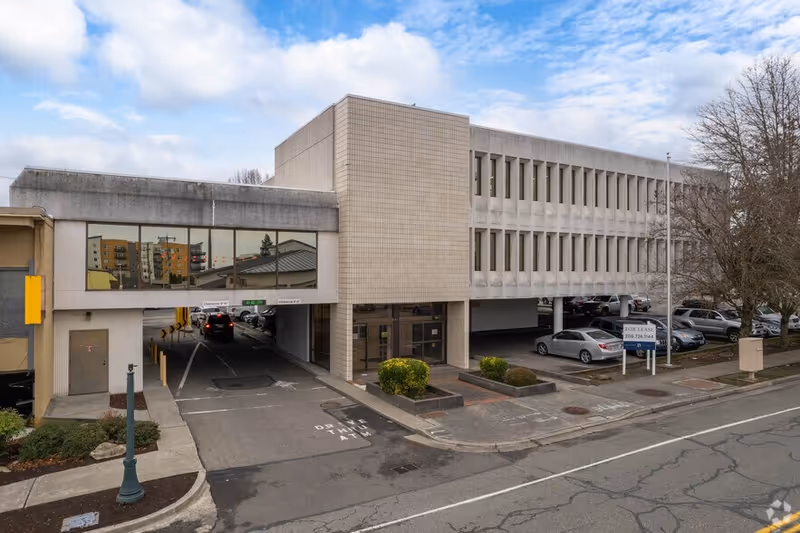 Exterior view of a multi-story concrete facility with drive-through entrance and parking.