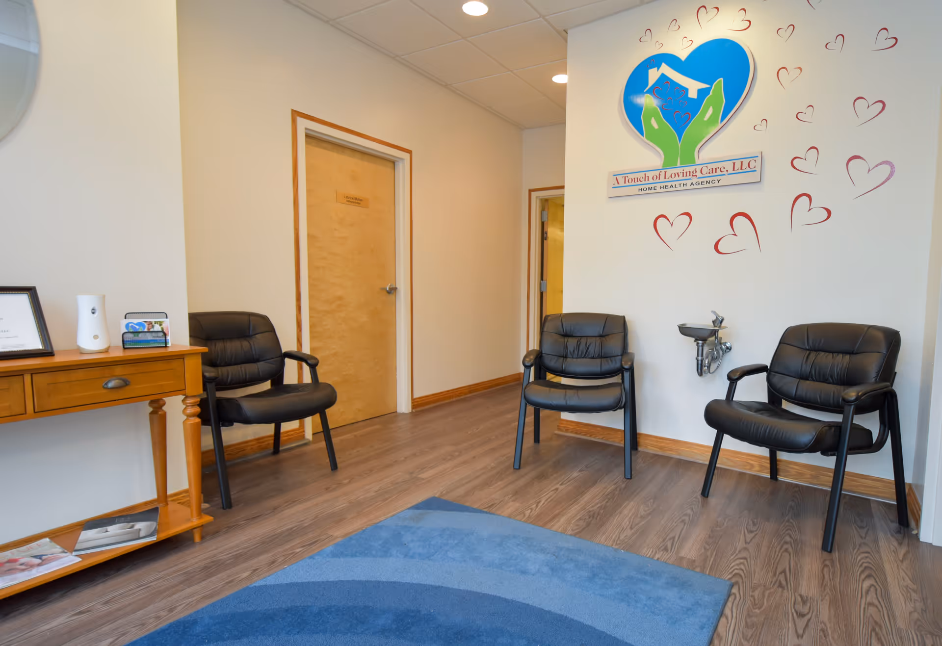 A waiting area with black chairs, a wooden console, and a heart-themed wall logo.