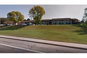 Exterior view of a long, low-rise retirement center with a grassy slope and parked cars.