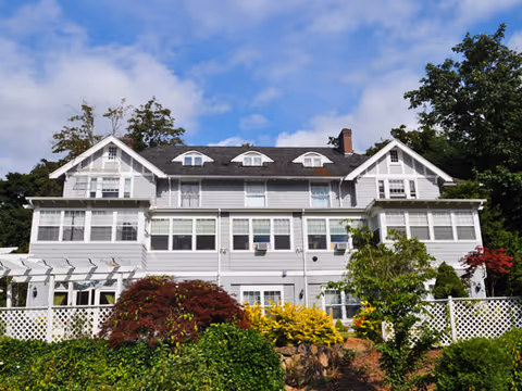 A large gray mansion-style senior living facility with dormer windows and a landscaped front garden.