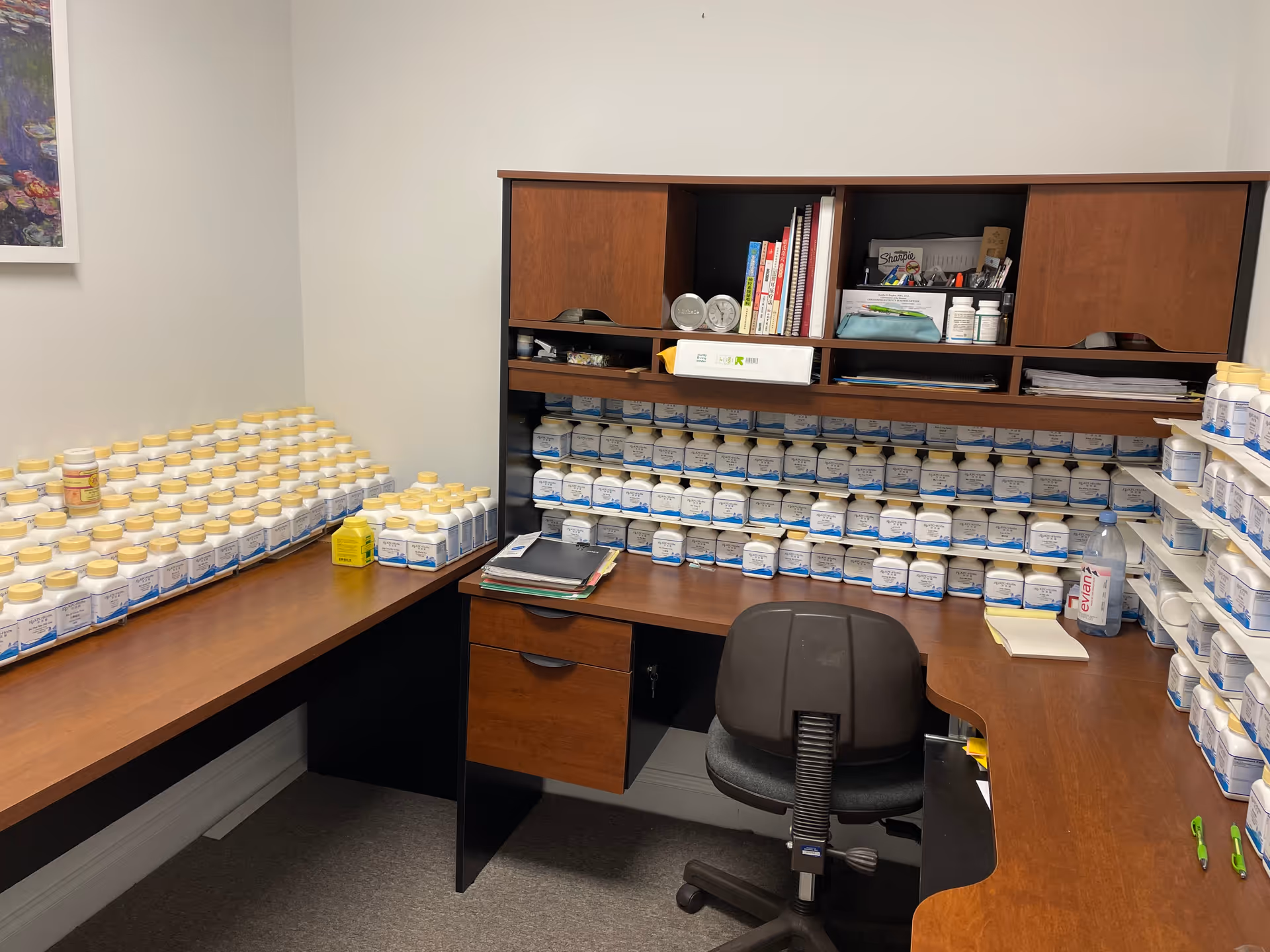 A corner office area filled with numerous labeled medicine bottles on shelves and a desk