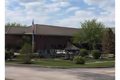 Front view of Thomson-Hood Veterans Center with flag, trees, and a parking lot.