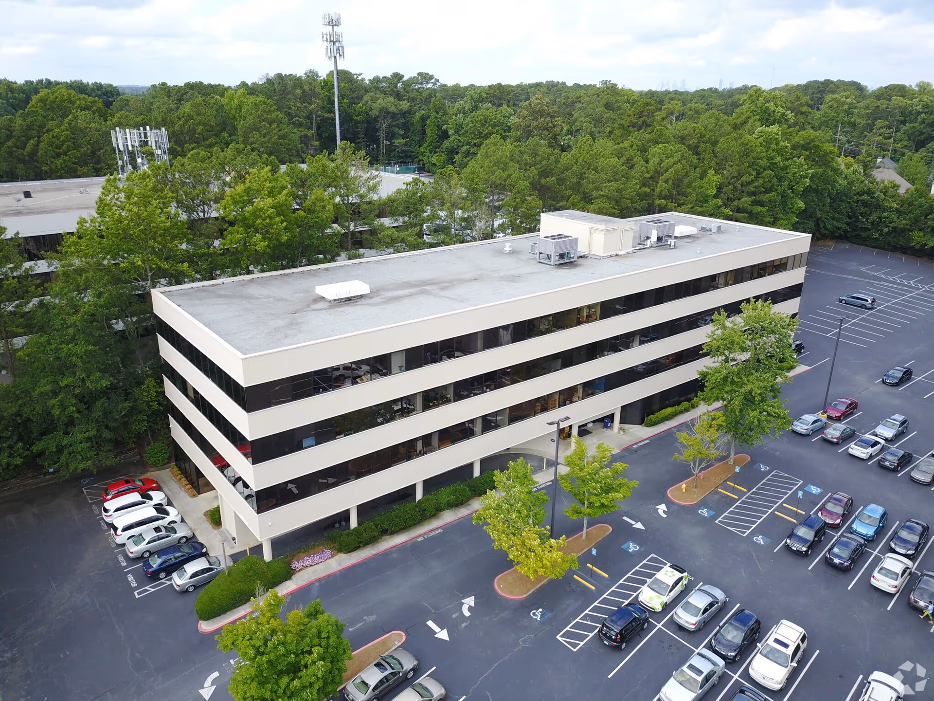 Aerial view of a beige, multi-story building with a surrounding parking lot and trees.