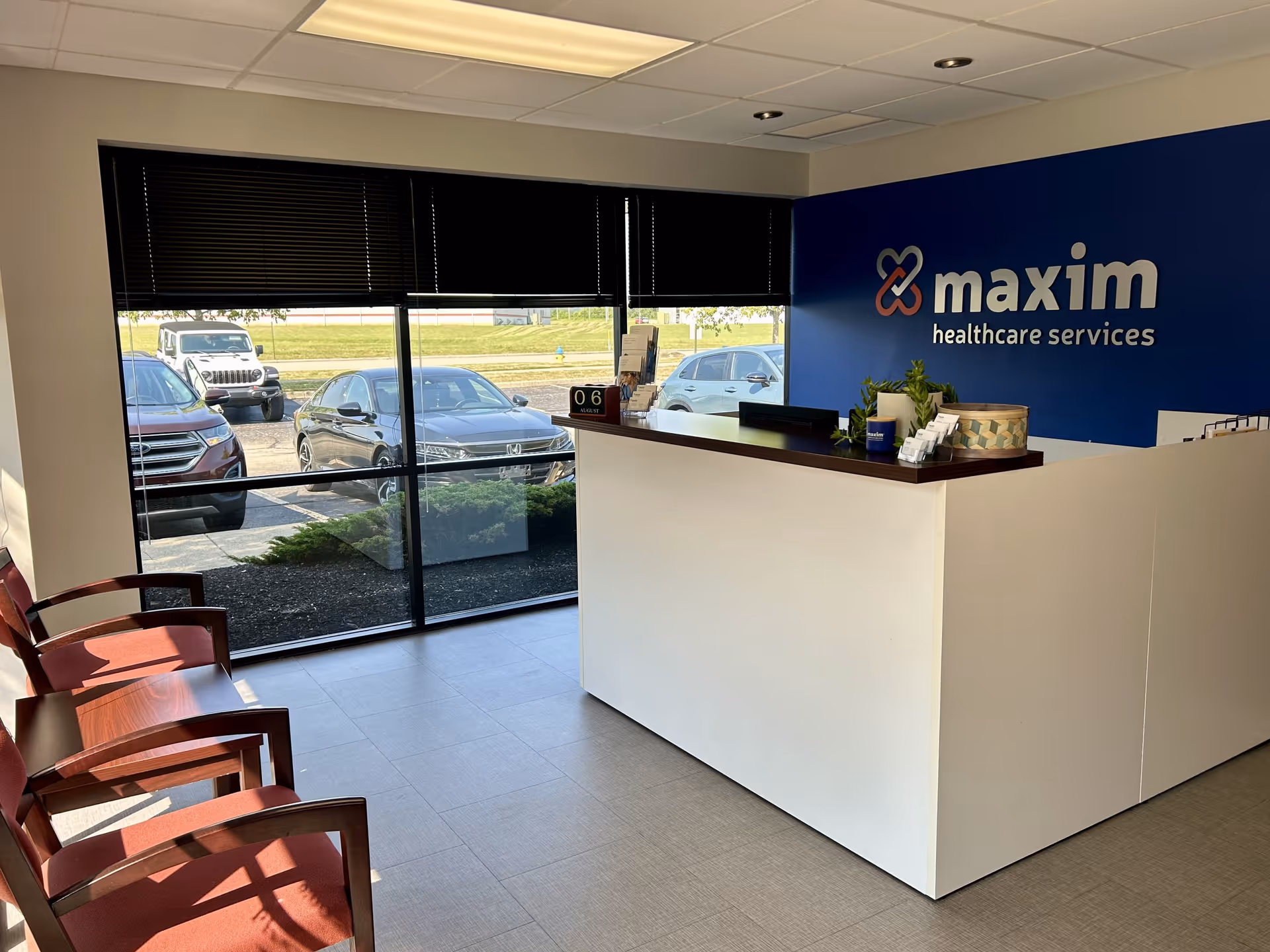 Reception area with white counter, blue Maxim wall, red chairs, and large windows
