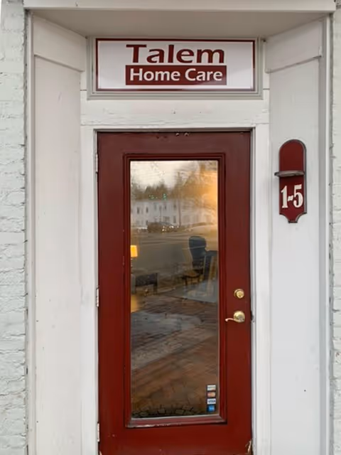 Front entrance of Talem Home Care, red door, white facade, street reflection in glass.