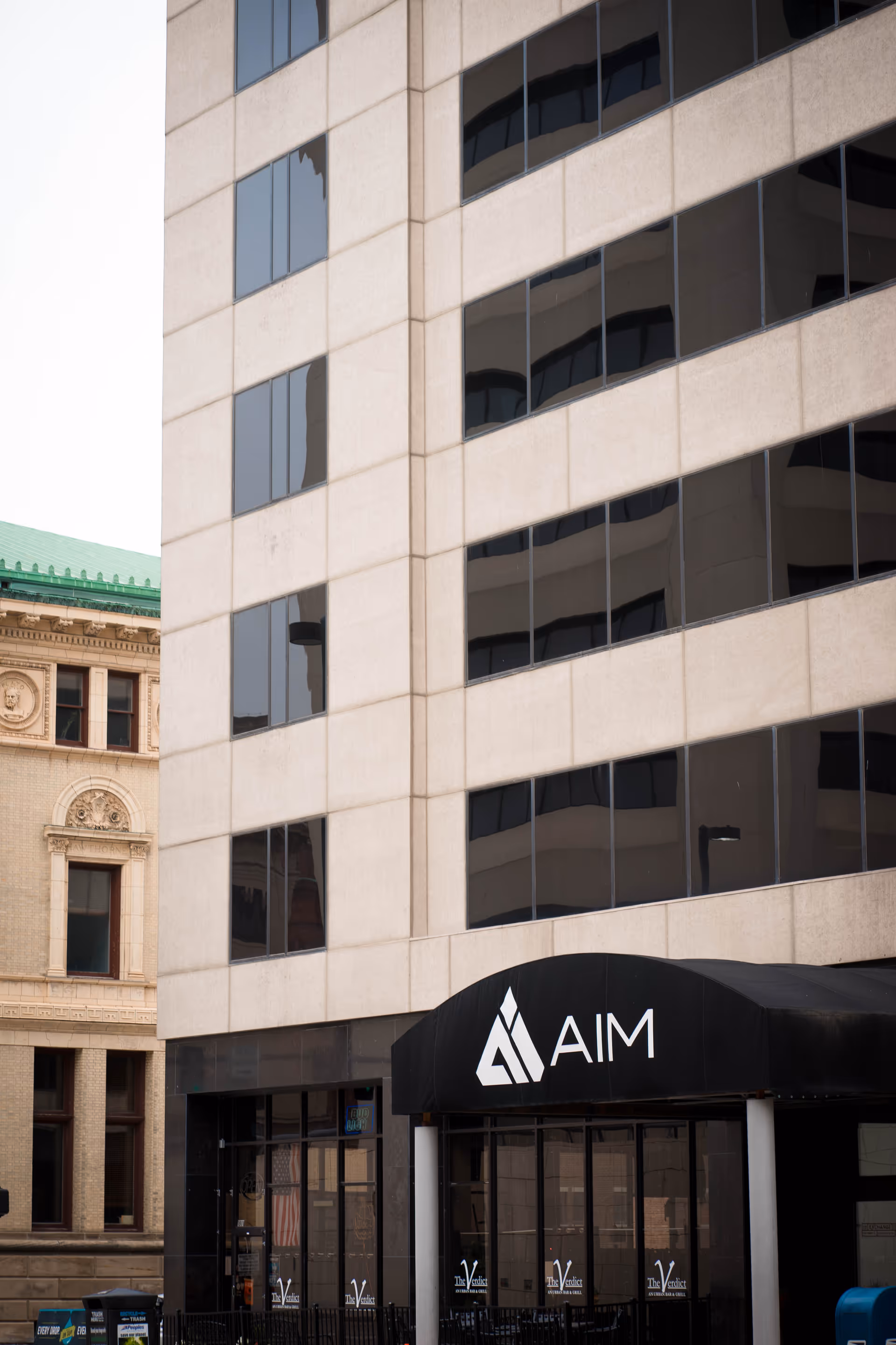 Tall modern building facade with large windows and a black awning at the entrance.