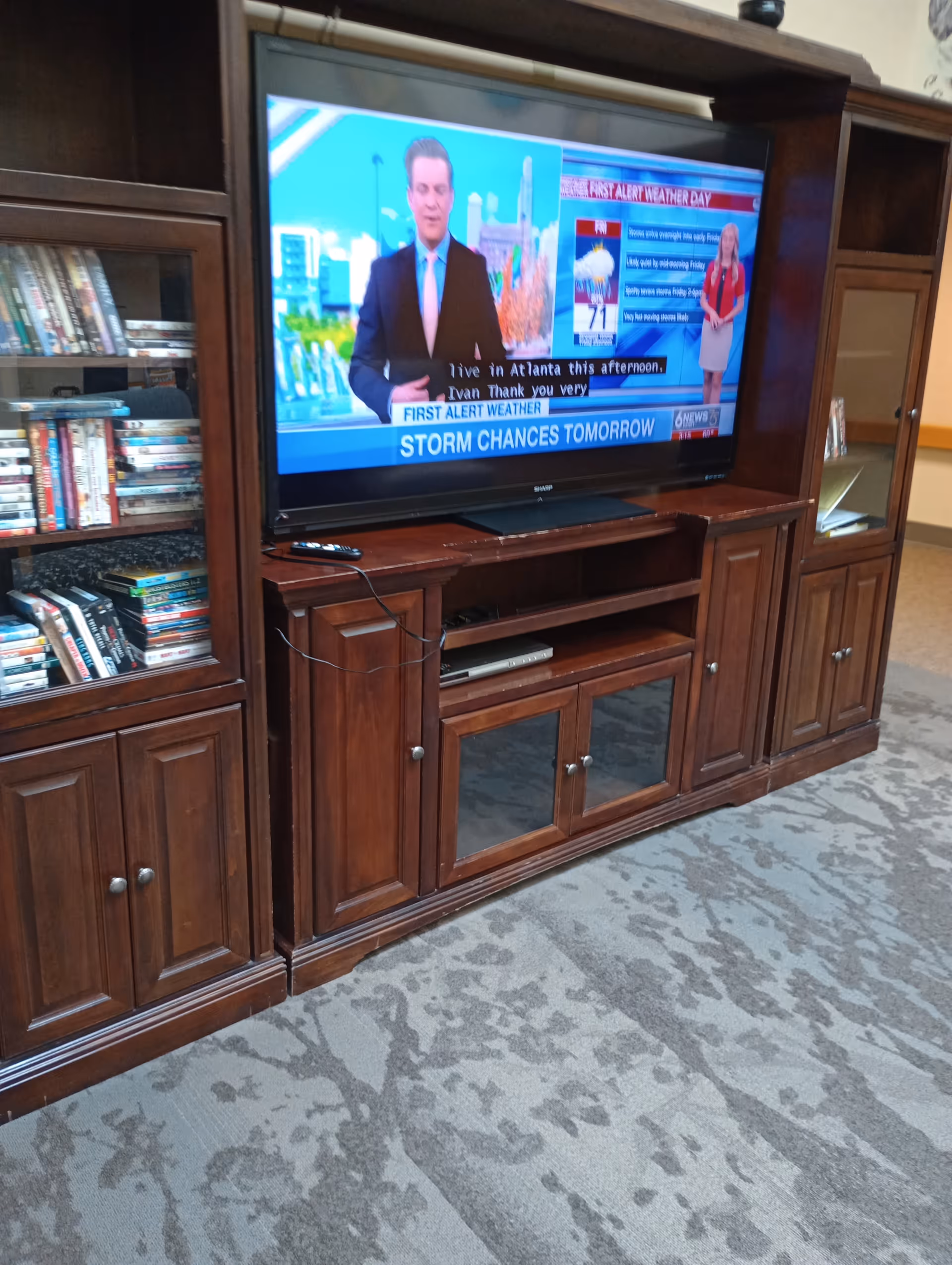 Wooden entertainment center with a large TV, bookshelves, and a remote in a carpeted living area