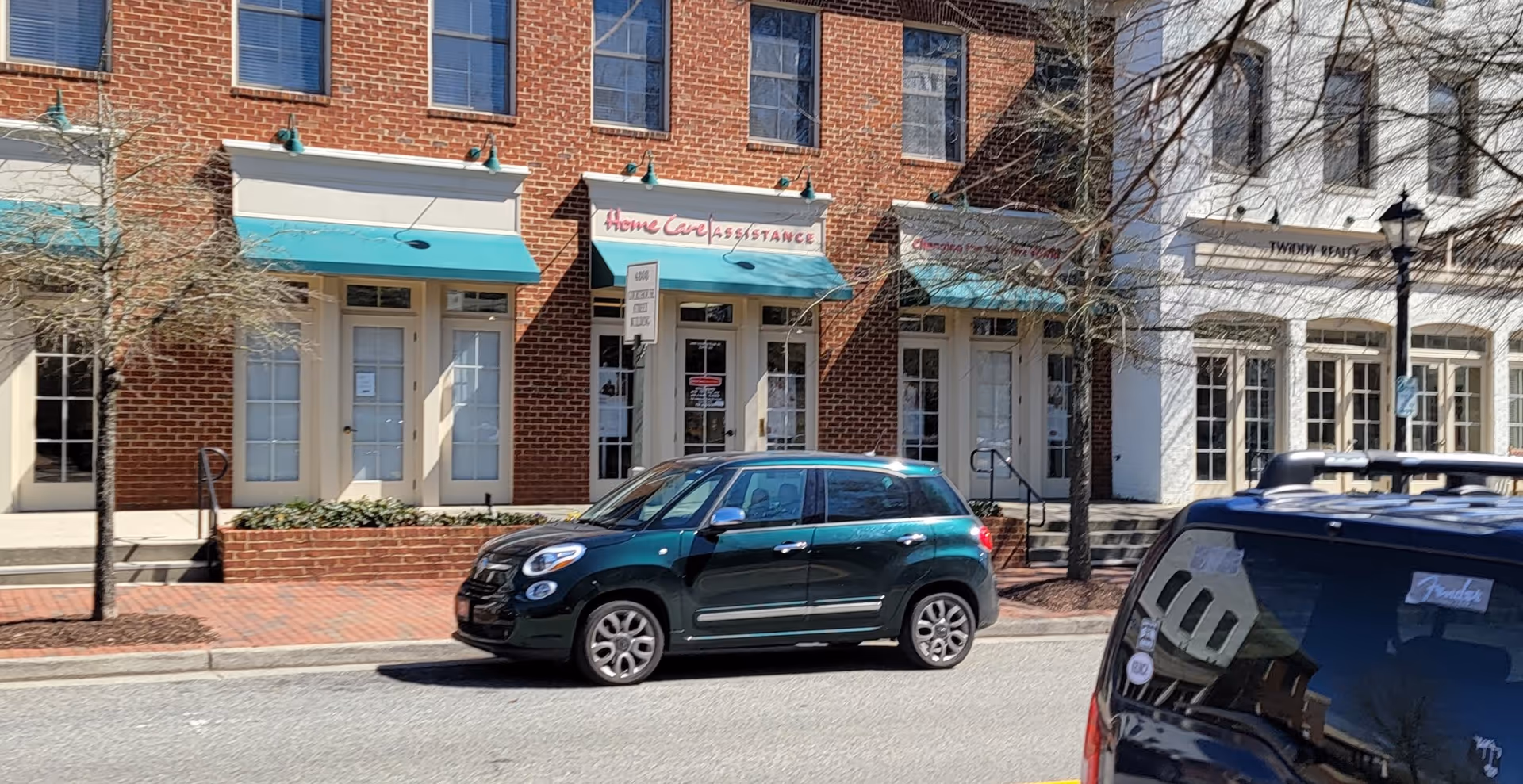 Street view of brick storefronts including Home Care Assistance signs and parked cars.