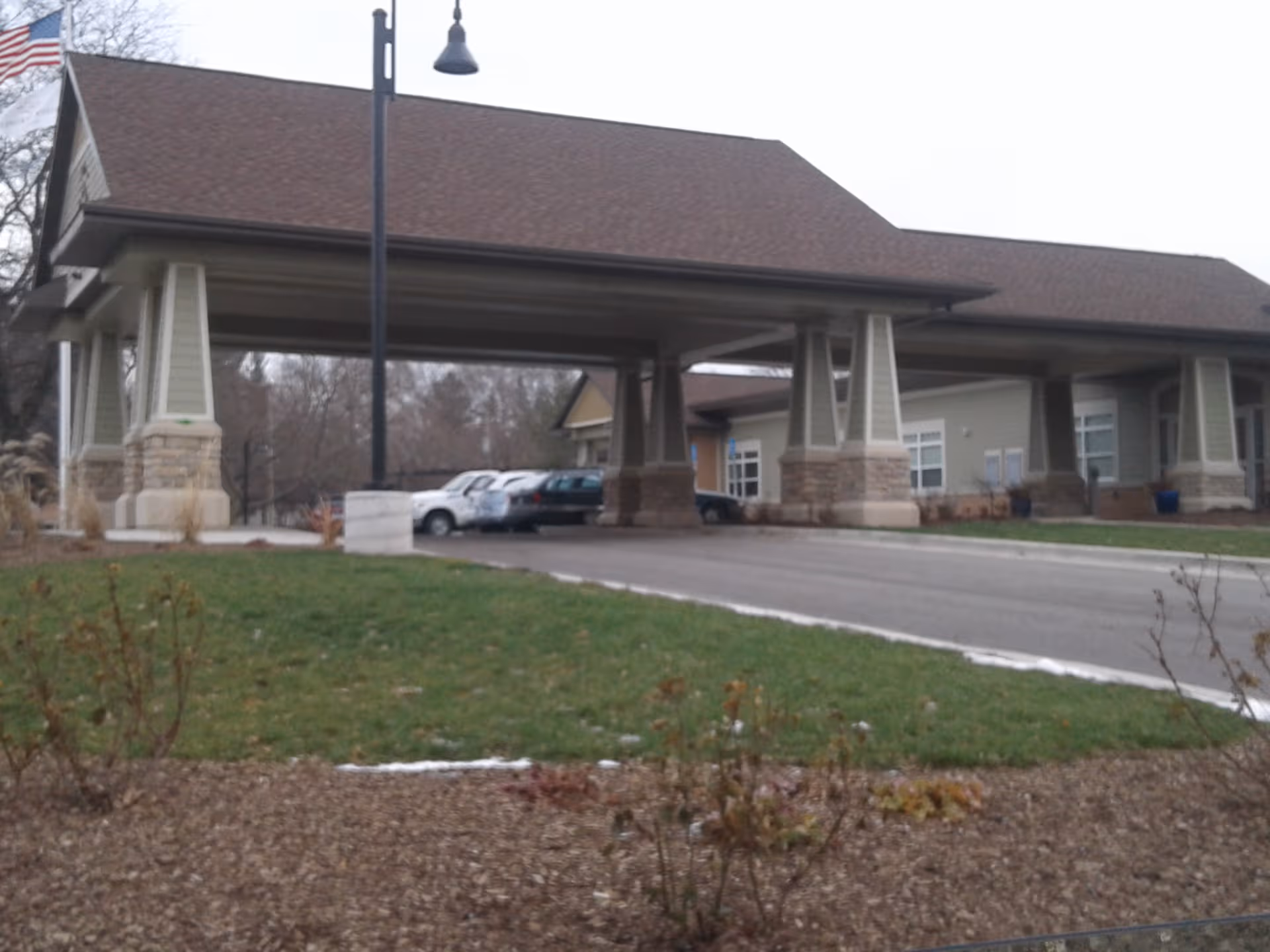 Exterior view of a facility entrance with a covered driveway and parked cars.