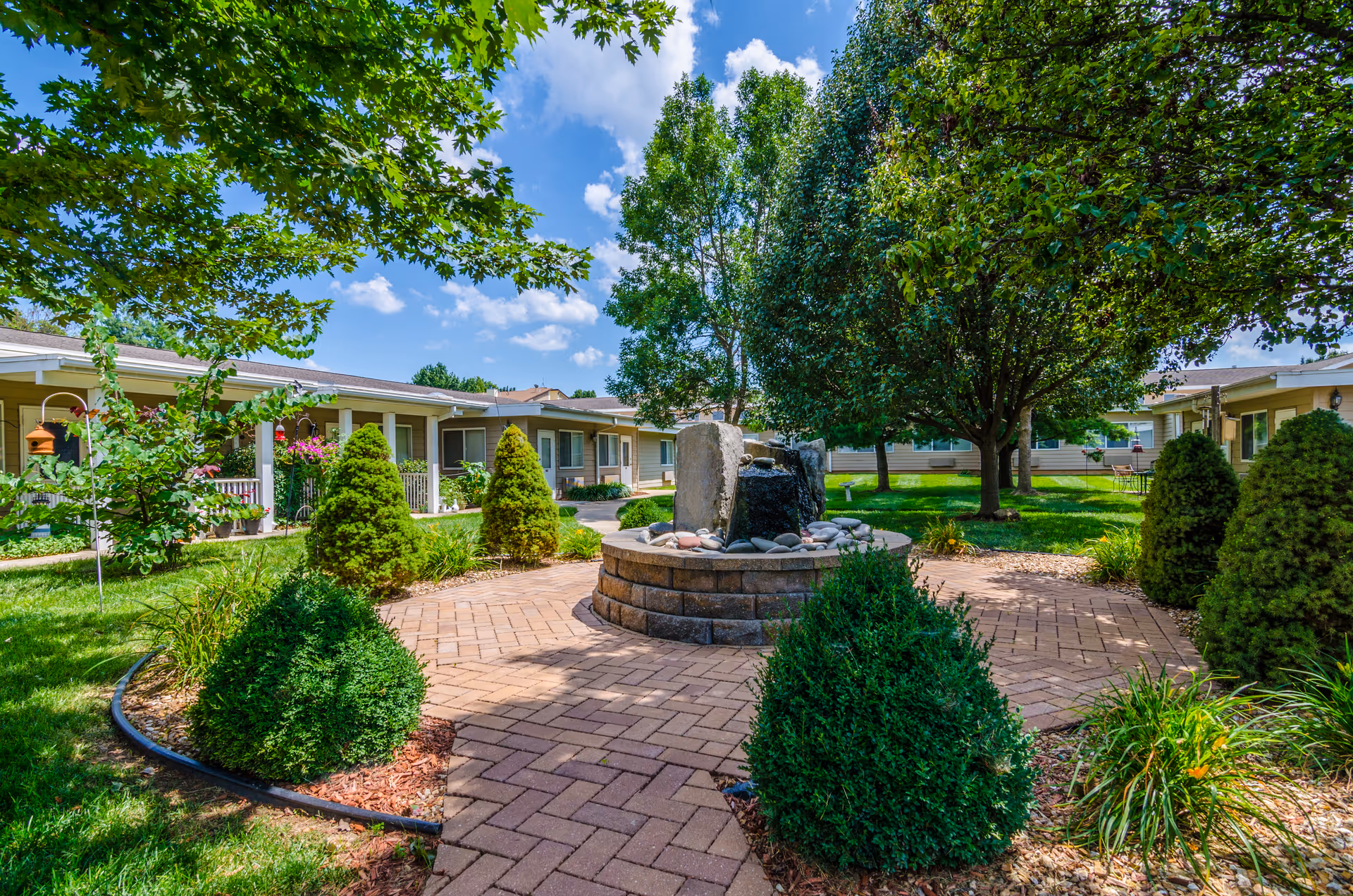 Well-kept courtyard with a central stone fountain, brick walkway, and manicured landscaping.