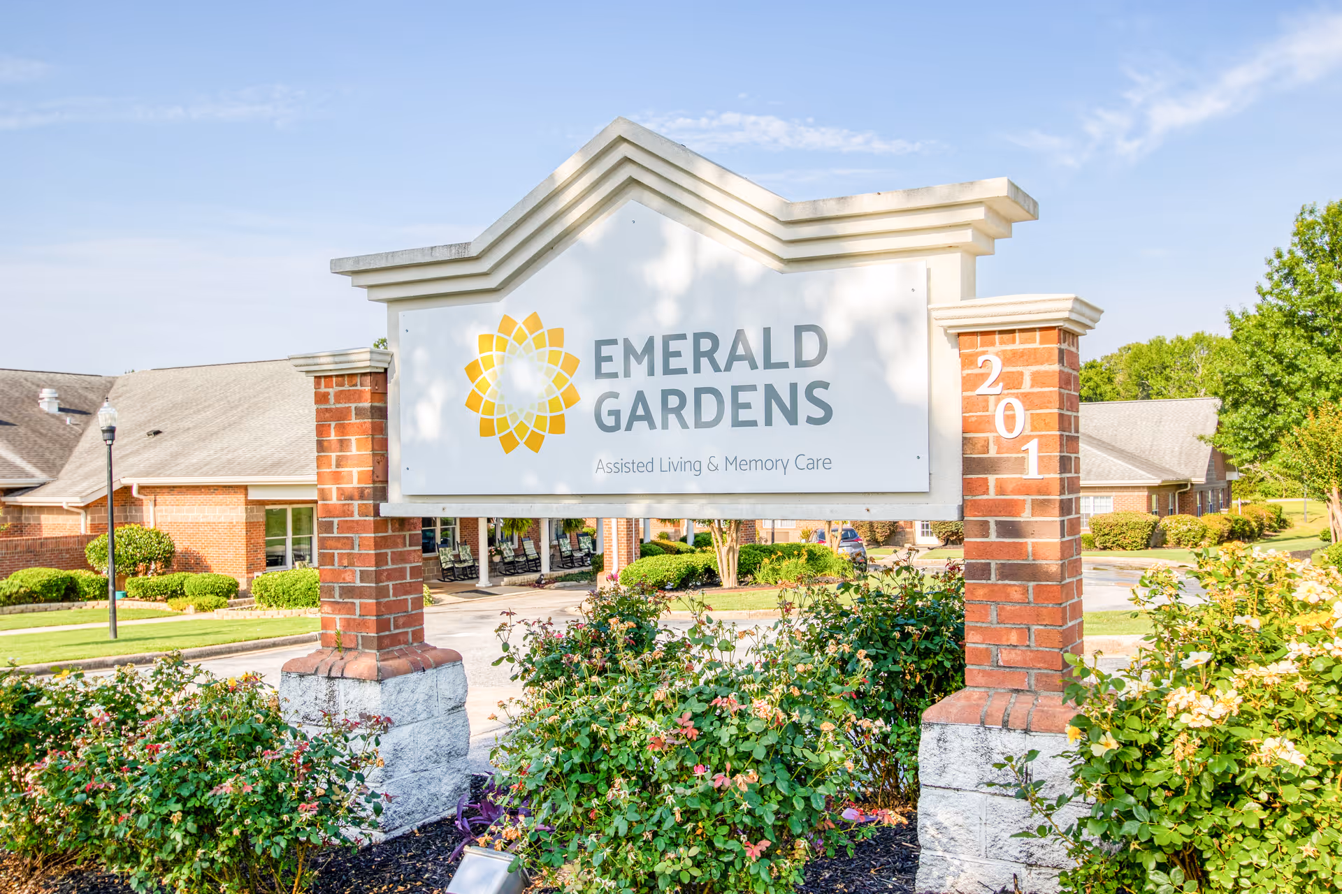 Front view of Emerald Gardens exterior sign with brick pillars and landscaped greenery.