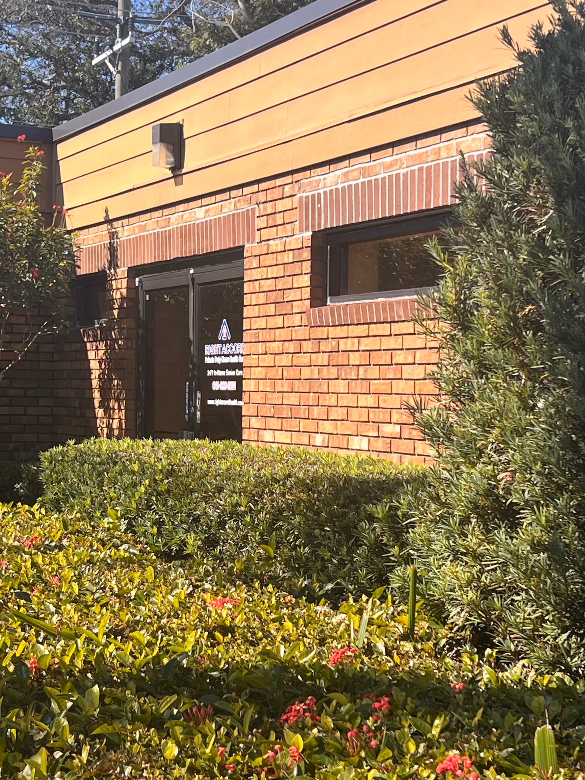 Exterior brick facility with glass entrance, sign, and landscaped shrubs.
