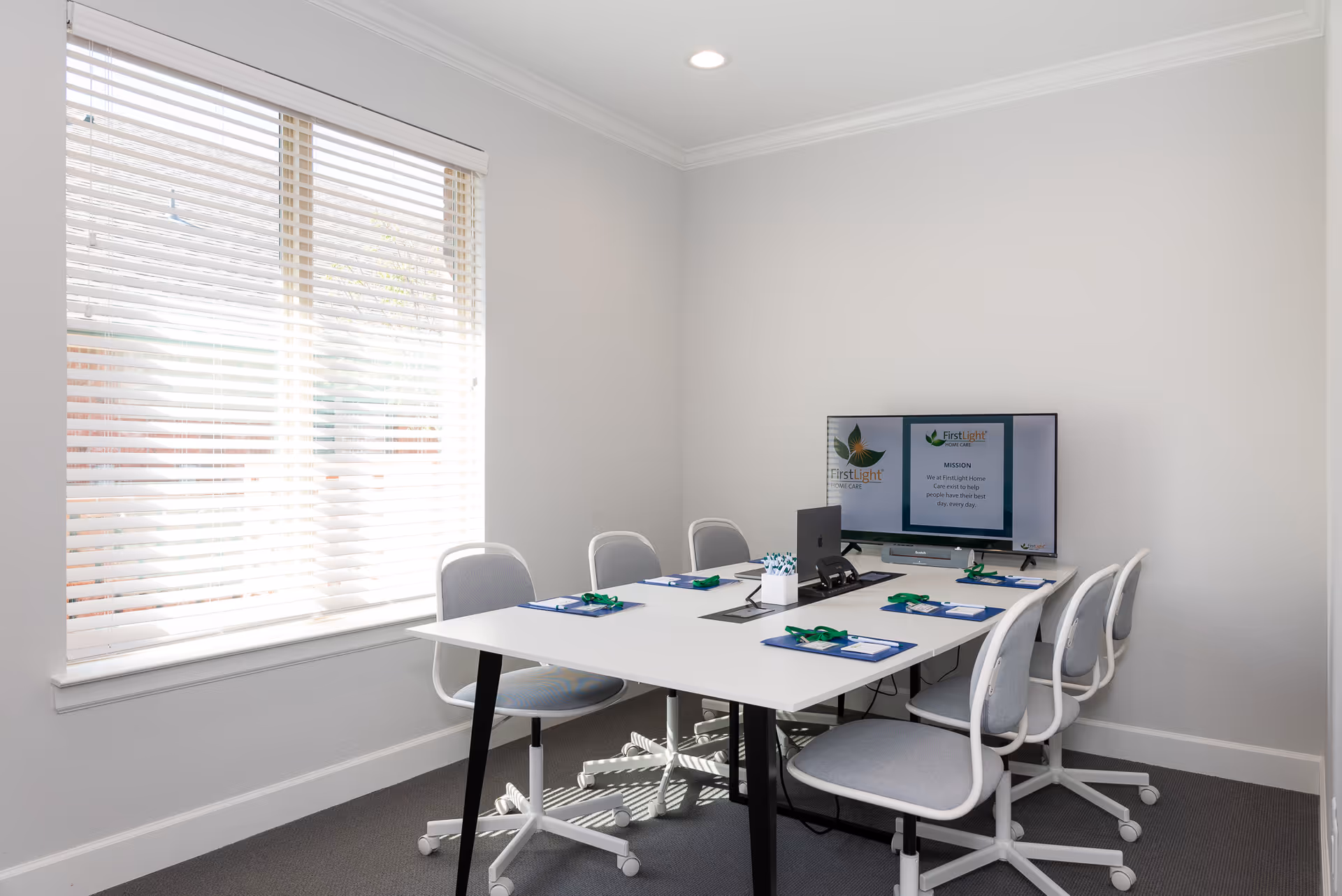 Small meeting room with white table, chairs, and a monitor displaying FirstLight logo.