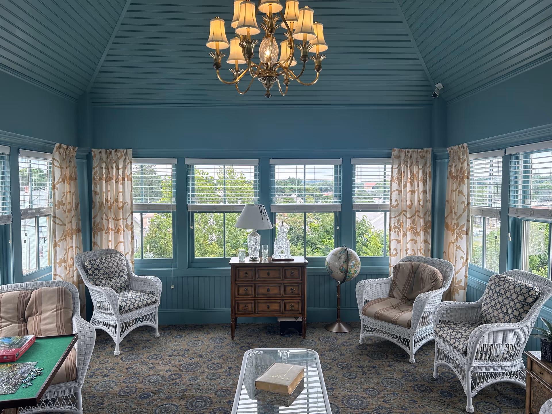 Teal sunroom interior with wicker chairs, a chandelier, and a glass coffee table.