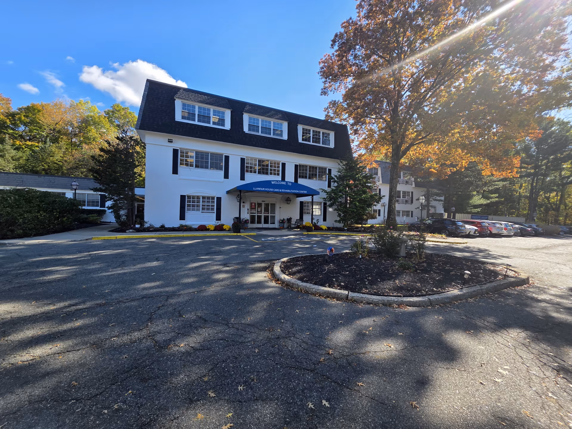 White three-story building with blue awning entrance, surrounded by parking and trees.