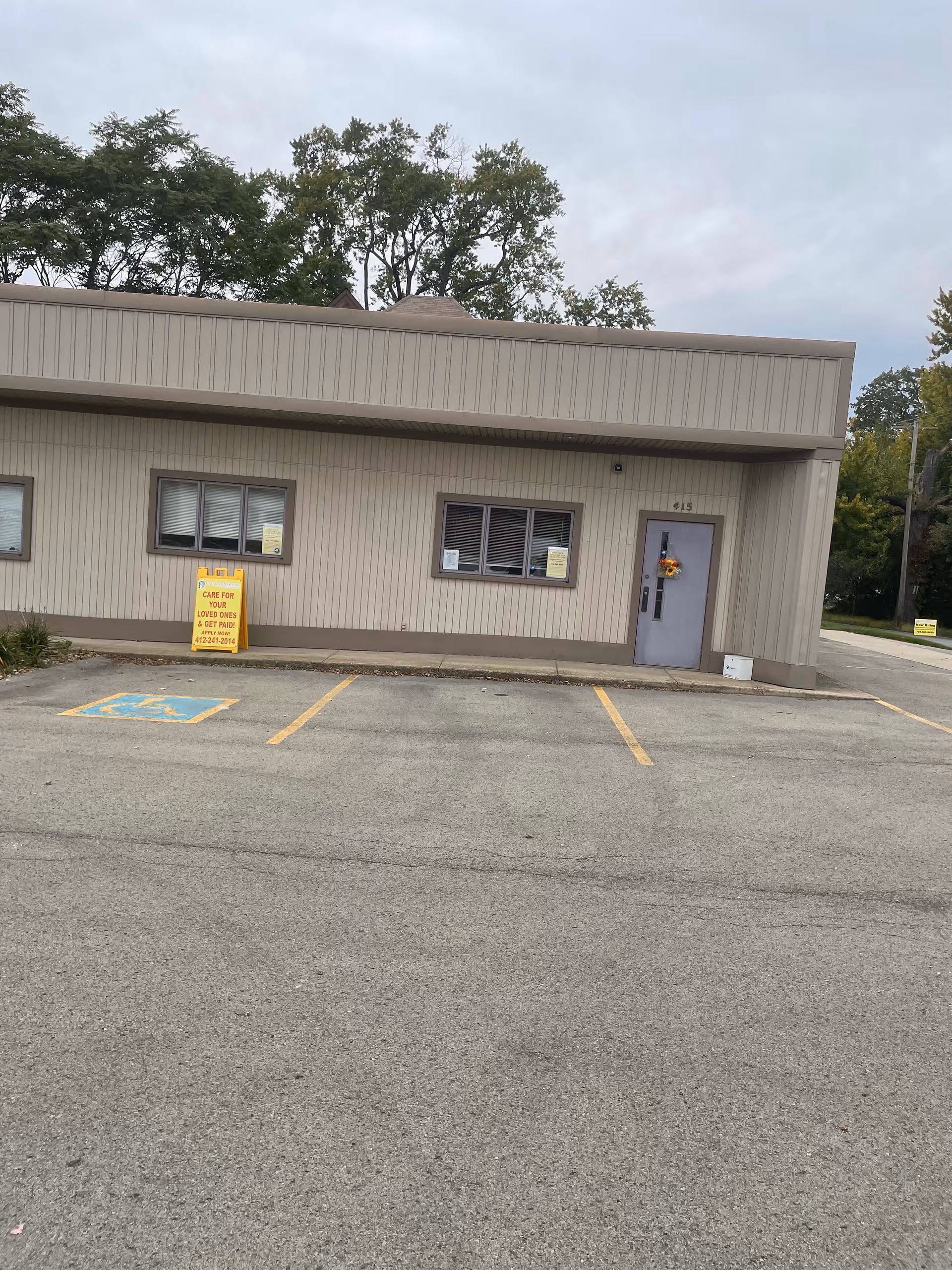 A single-story beige facility front with a door and adjacent parking area.