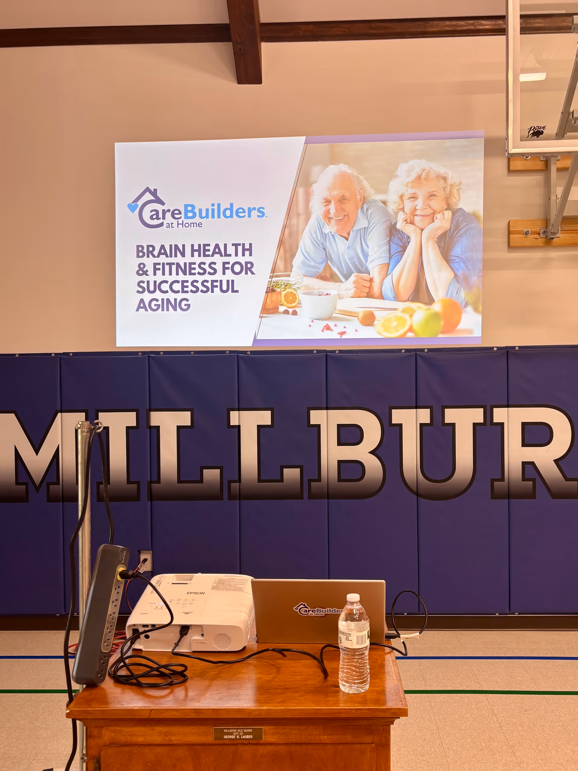Interior gym-style room with a CareBuilders banner, projector, laptop, and water bottle.