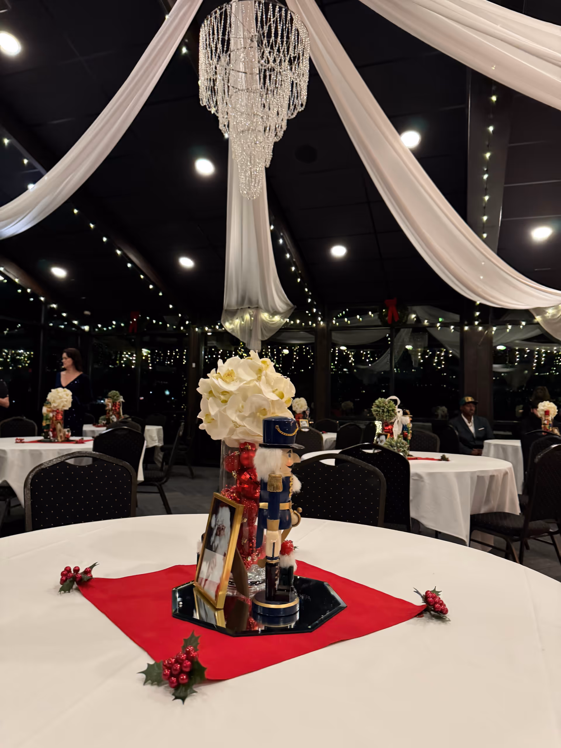 Indoor banquet hall with draped white fabric, chandeliers, and decorated round tables.