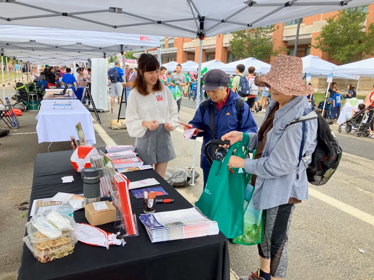 People browse tables under white canopies at an outdoor community event.
