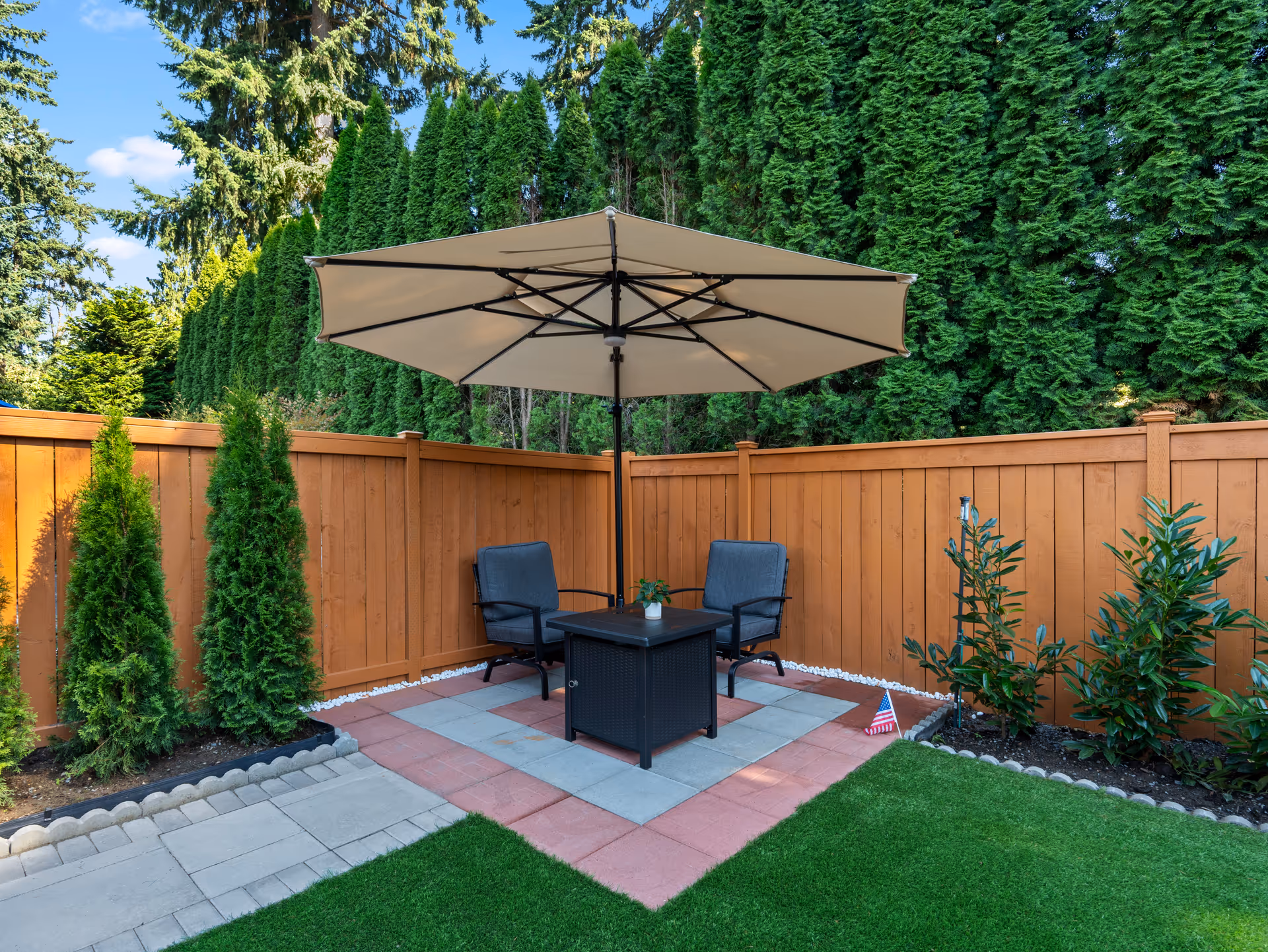 Patio seating area with table and umbrella, bordered by a wooden fence.