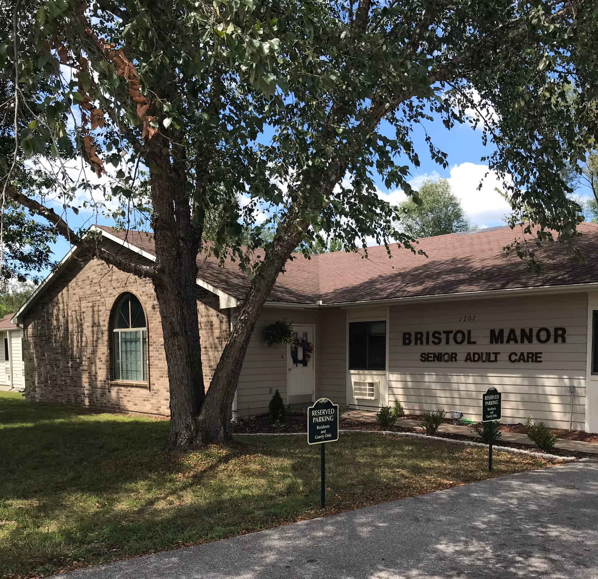 Exterior view of Bristol Manor Senior Adult Care with tree in foreground