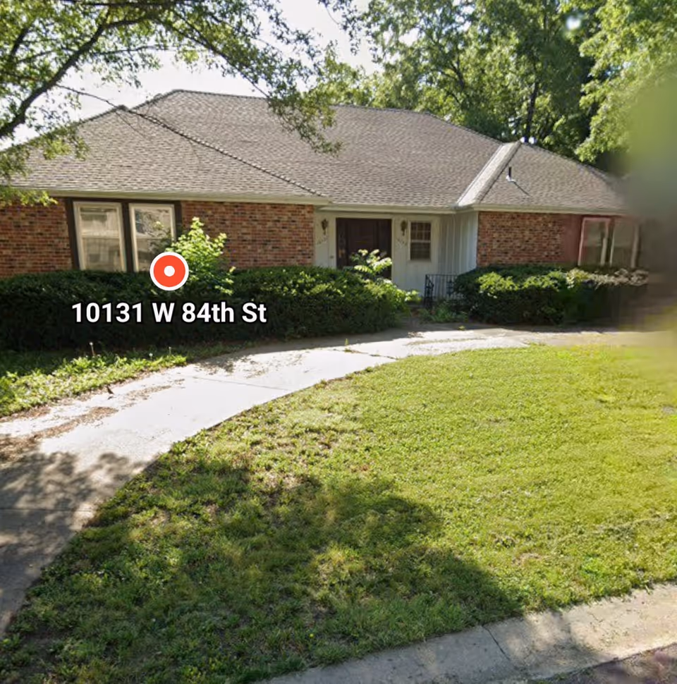 Brick, single-story building front with curved sidewalk and hedges.