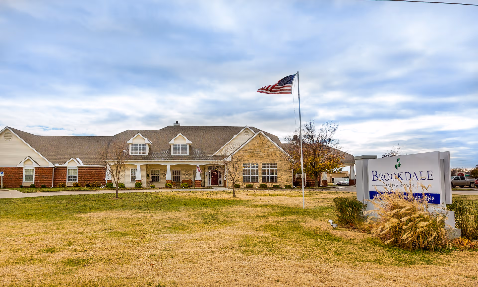 Exterior view of Brookdale Salina Kirwin facility with entrance, sign, flag, and manicured lawn.