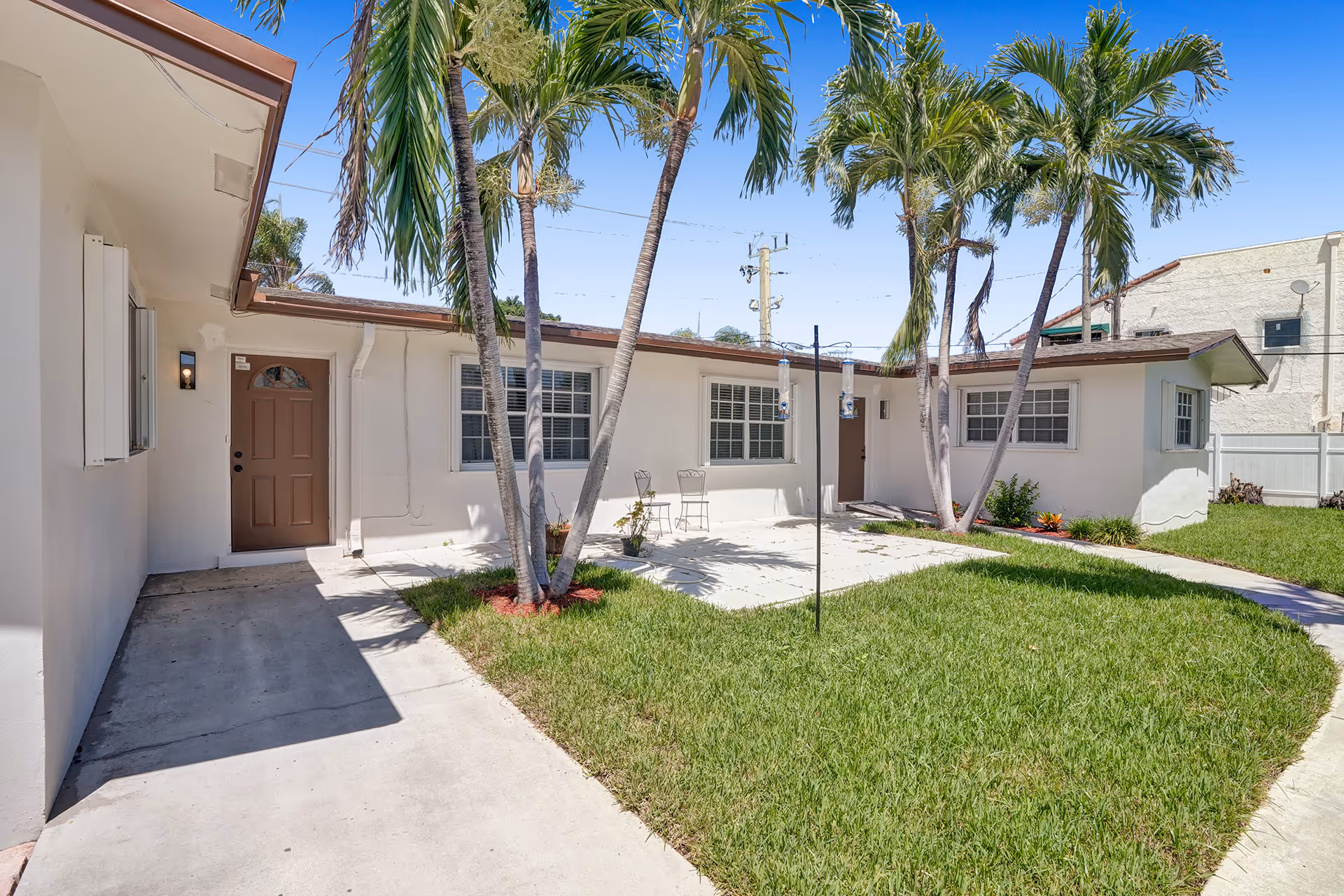 Single-story beige senior care facility exterior with palm trees, entry doors, and a grassy courtyard.