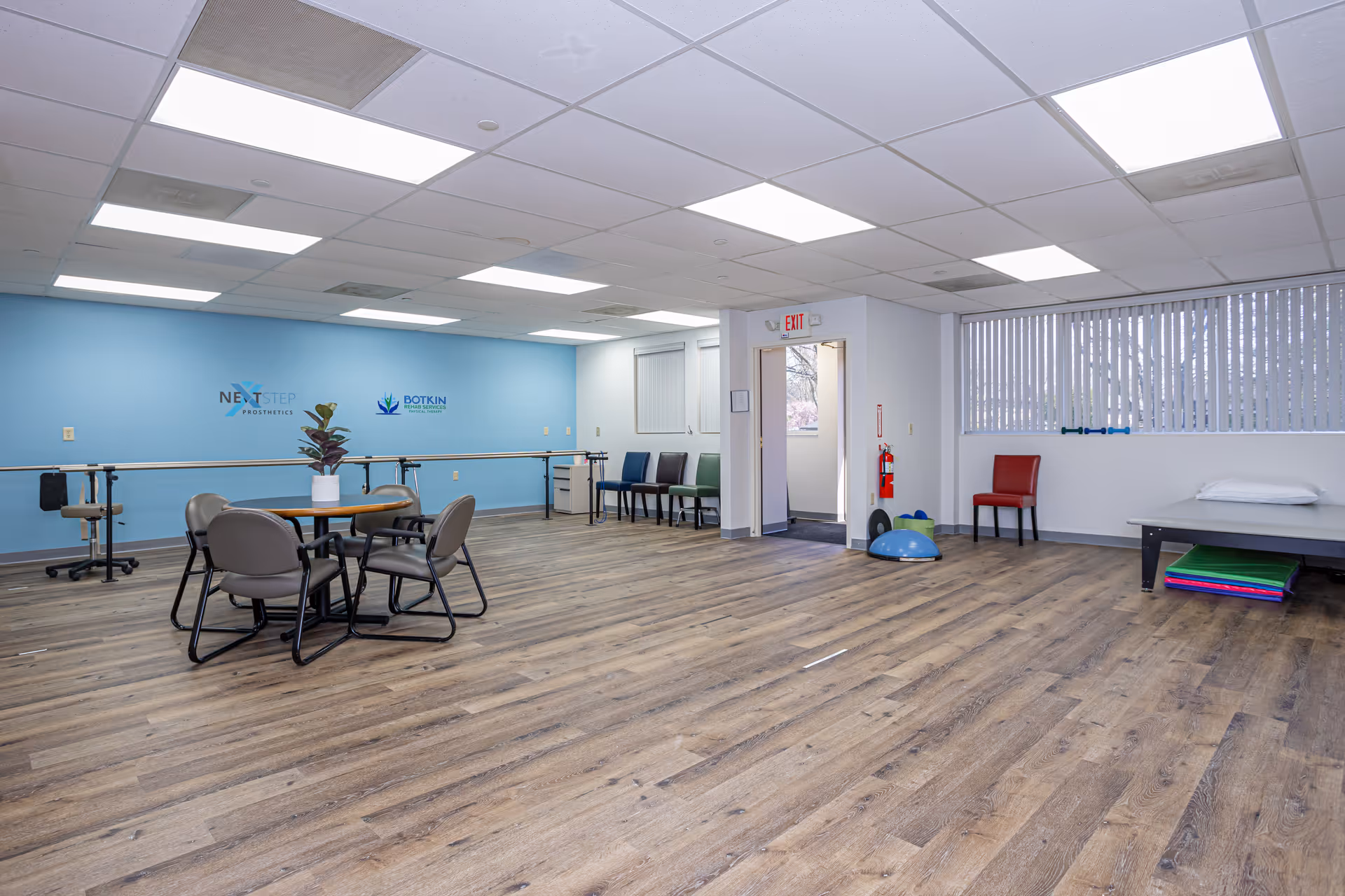 Bright therapy room with blue accent wall, tables, chairs, and exercise equipment.