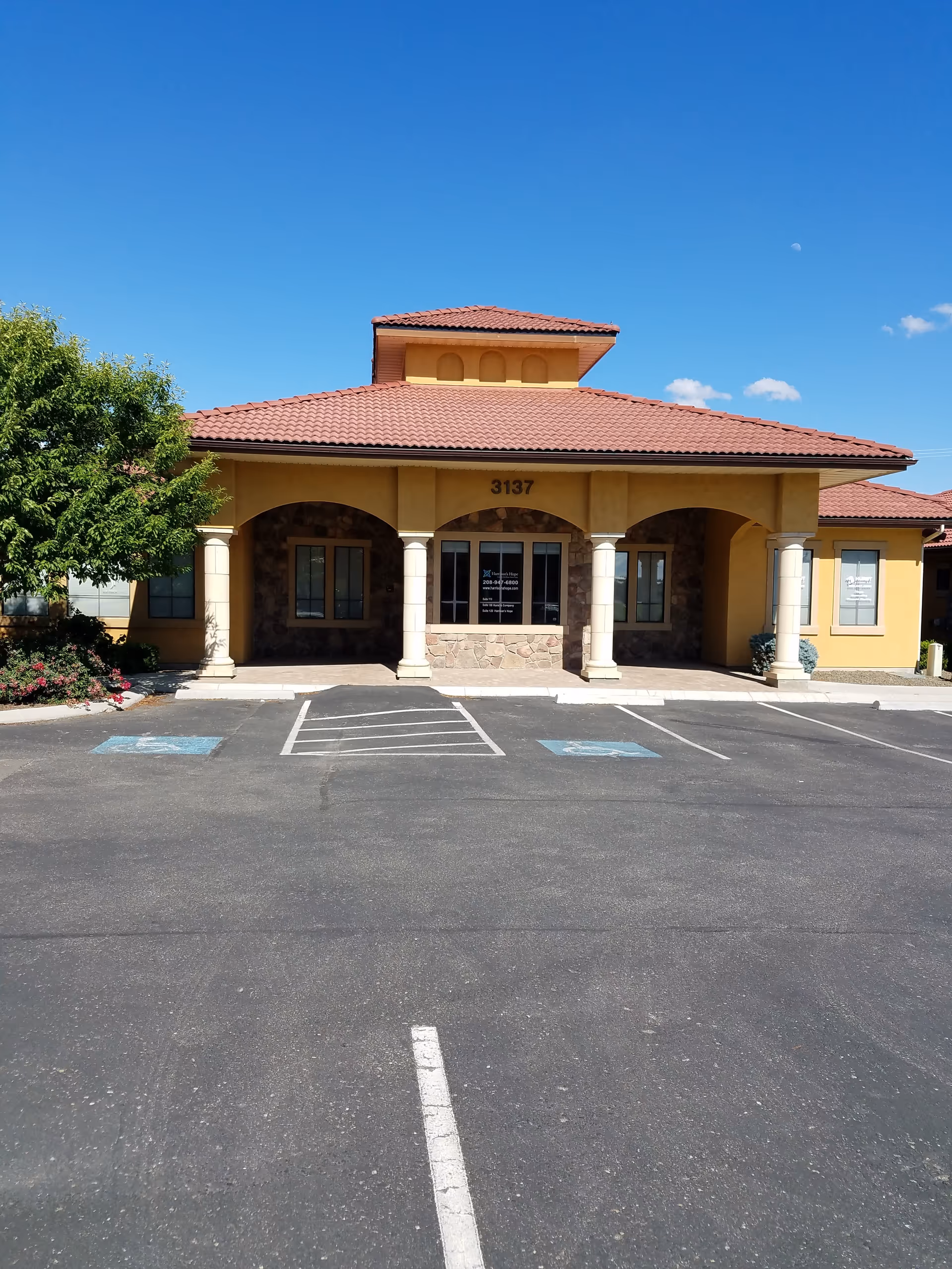 Senior living facility building front with arches, columns, and a parking lot on a clear day.