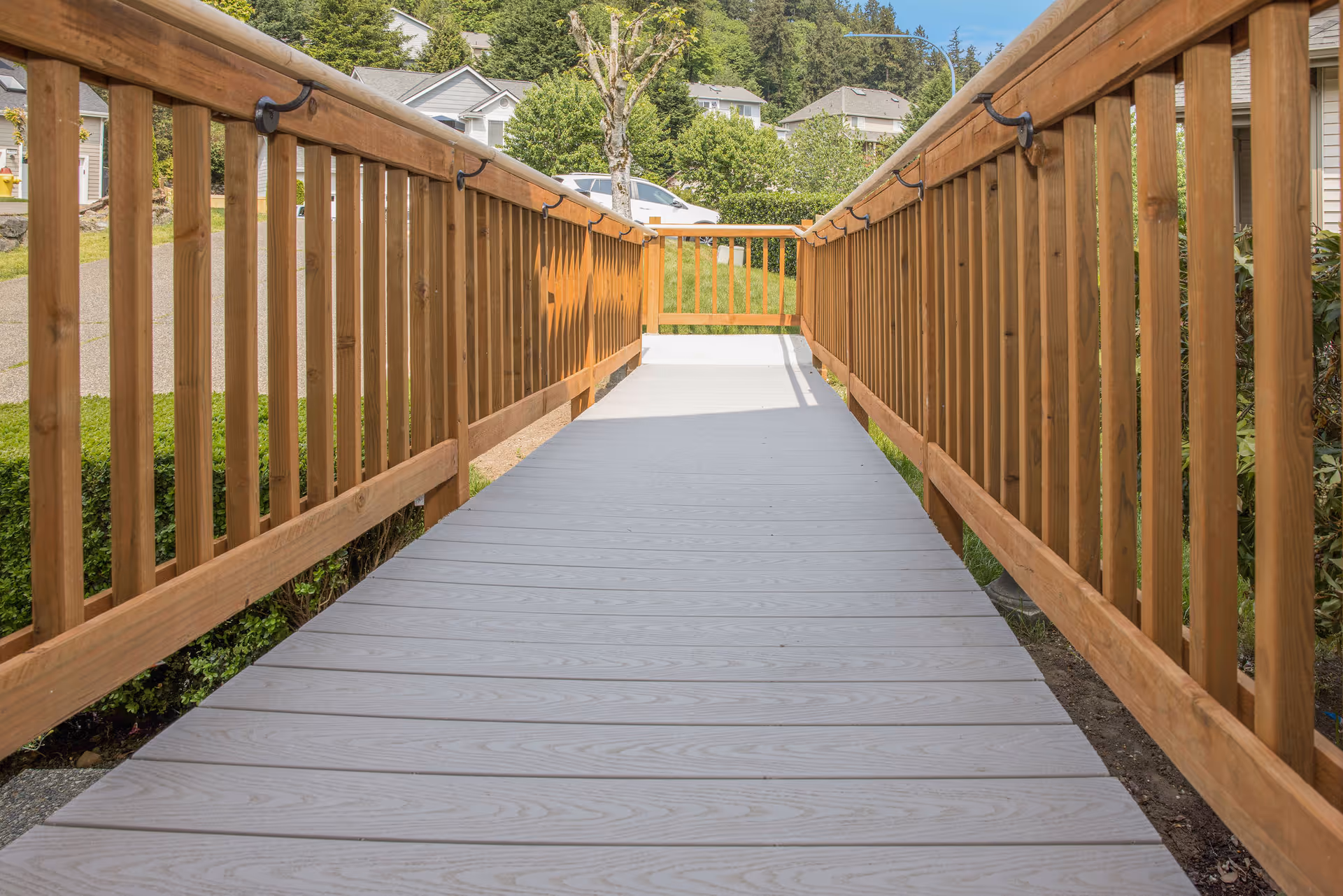 Outdoor wooden ramp leads to building entrance, flanked by railings and greenery.