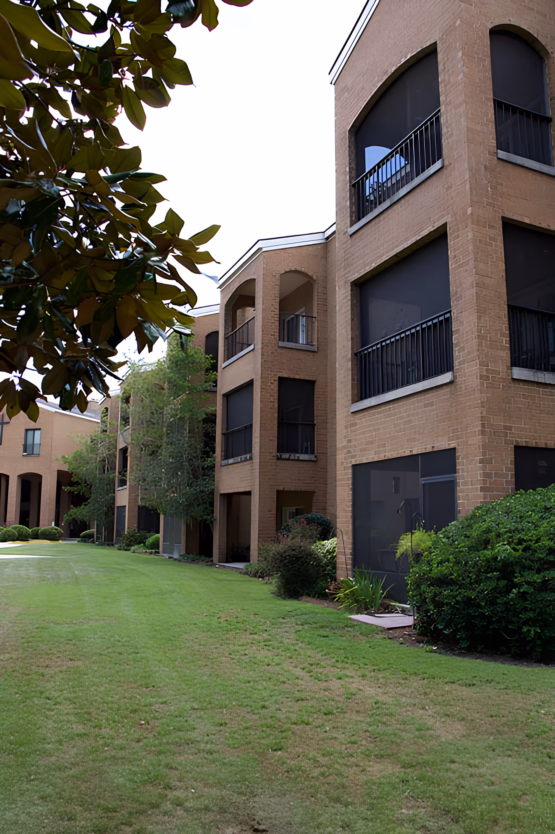 Exterior view of a brick senior living building with screened balconies overlooking a grassy courtyard.