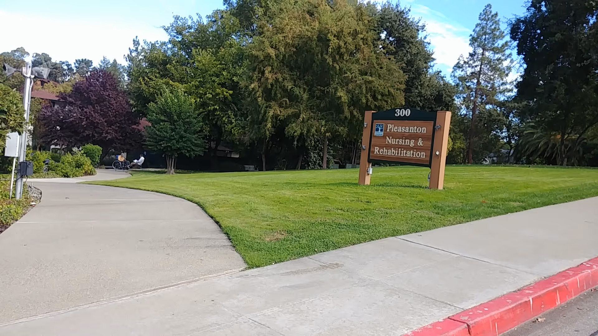 Pleasanton Nursing & Rehabilitation sign sits on a grassy lawn beside a curved sidewalk.