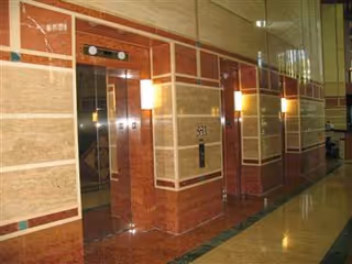 Luxurious marble hallway with elevator doors and warm wall sconces in a senior living lobby.