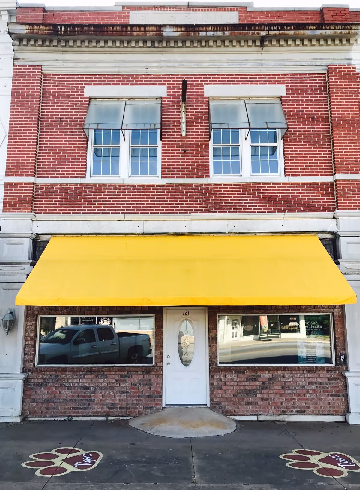 Brick building storefront with a yellow awning, two windows, and a white door.