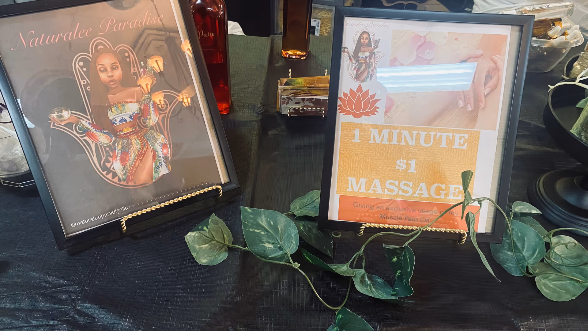 Two framed Naturalee Paradise posters on a black table with green ivy garlands.
