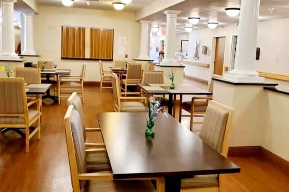 Dining room with wooden tables and upholstered chairs, decorative columns, and small vases on the tables.