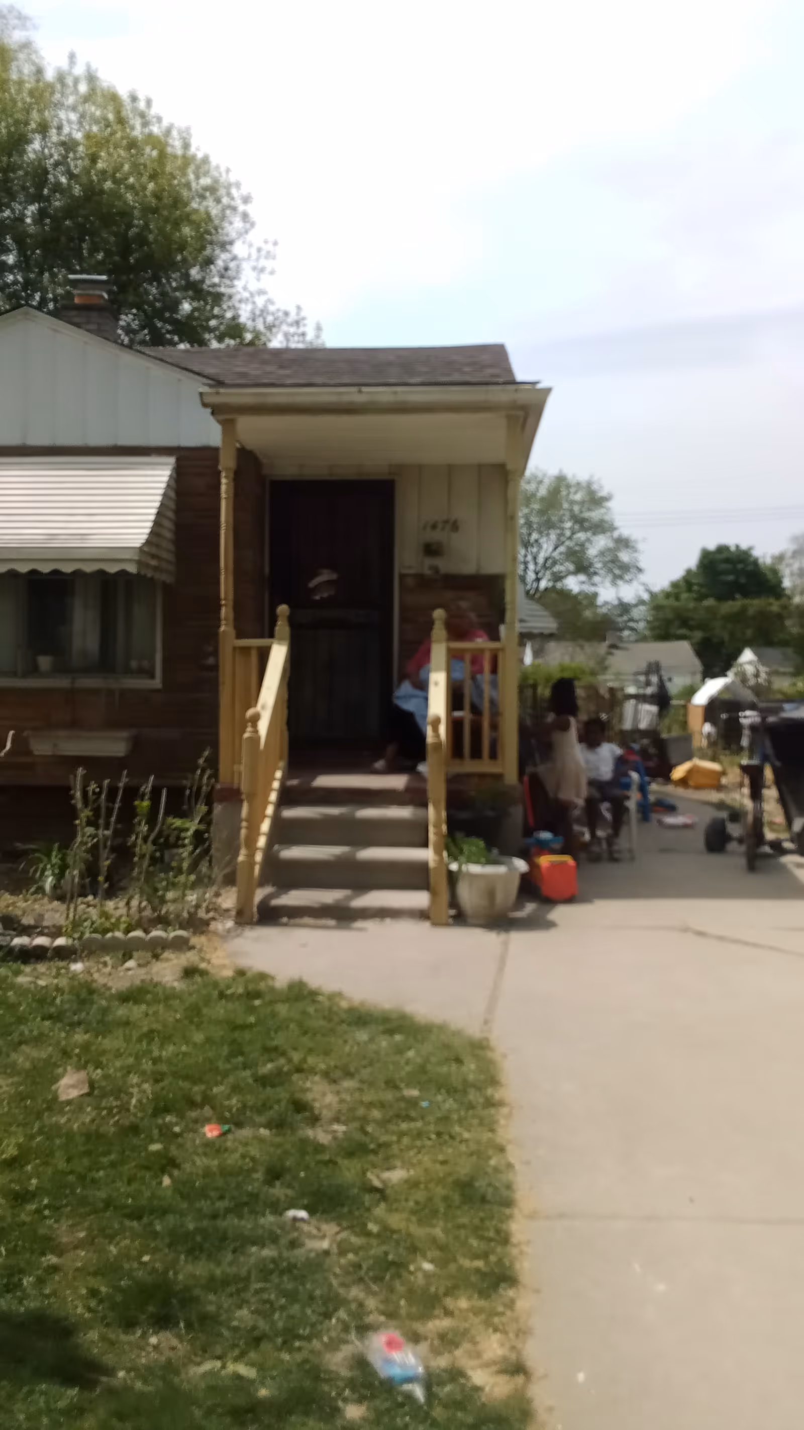 Small house exterior with a front porch, stairs, and people gathered outside.