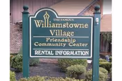 Green sign reads Williamstowne Village Friendship Community Center Rental Information, with shrubs in front.