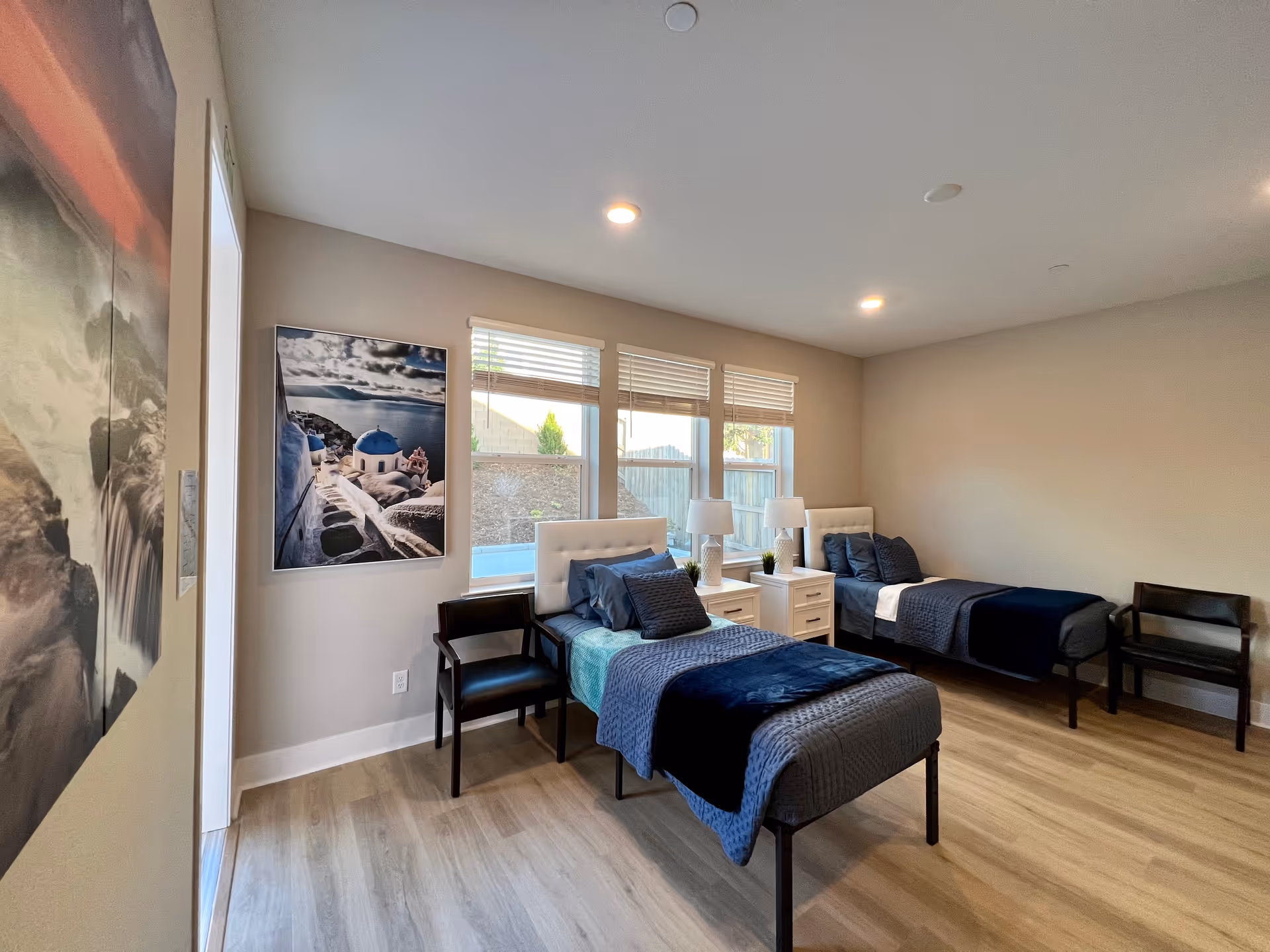 Two single beds with blue bedding and white nightstands in a bright bedroom.