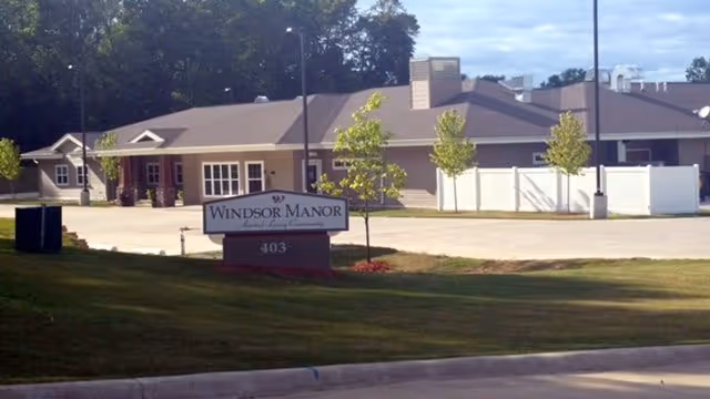 Front exterior of a single-story building with a lawn and a roadside sign reading 'Windsor Manor' and the number 403.