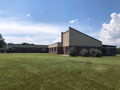 Single-story brick and stucco building with a large grassy lawn under a blue sky.