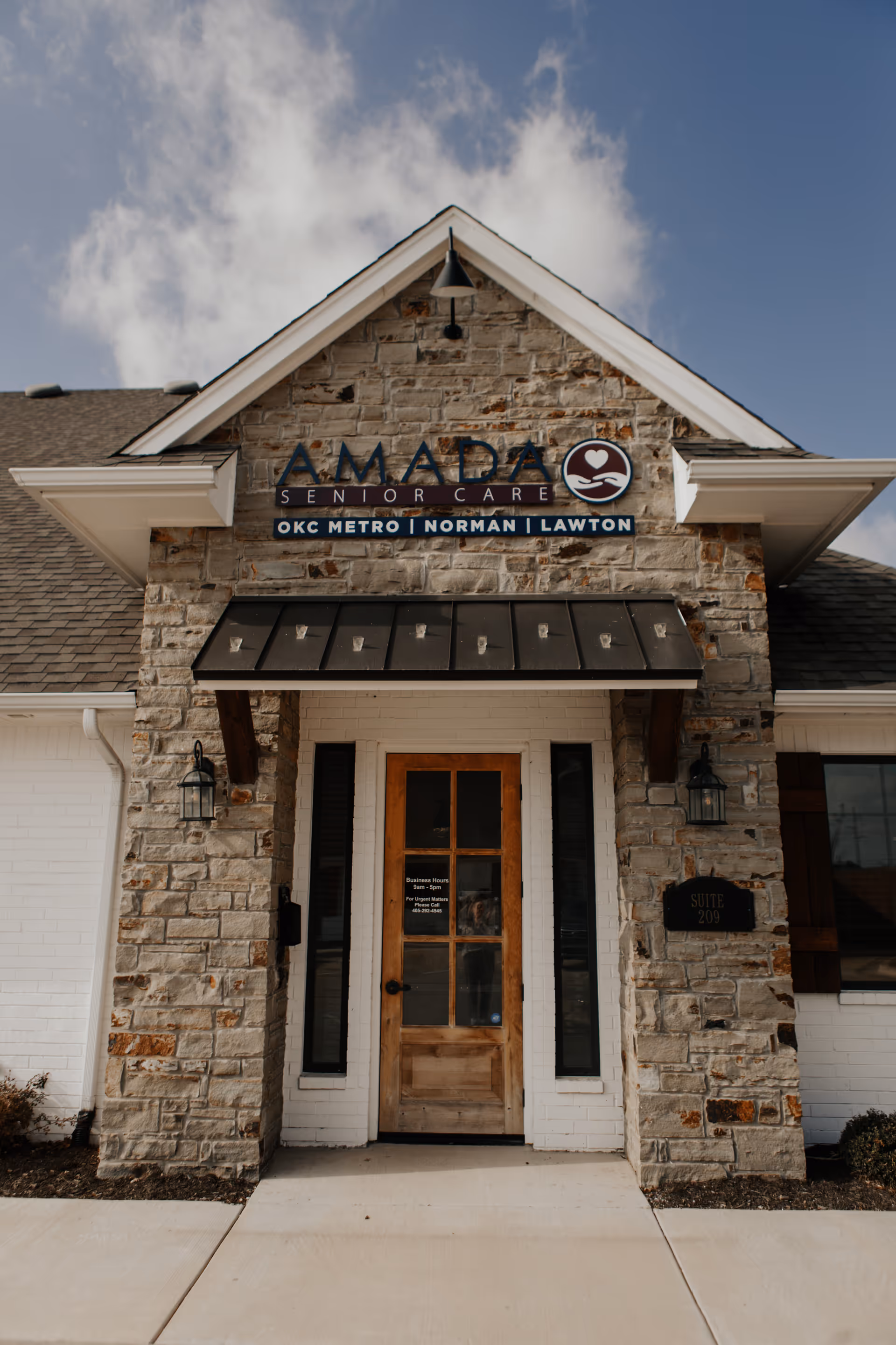 Stone façade with Amada Senior Care sign, wooden door, and entry pillars.