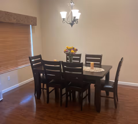 A dining room featuring a dark wood table, six chairs, flowers, and a chandelier.