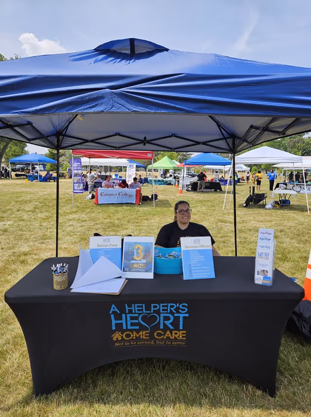 Outdoor booth for A Helper's Heart Home Care with a staff member and tents