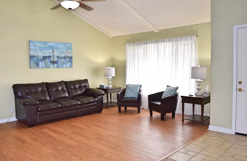 Bright living room in a senior living facility with leather sofa, chairs, and lamps.