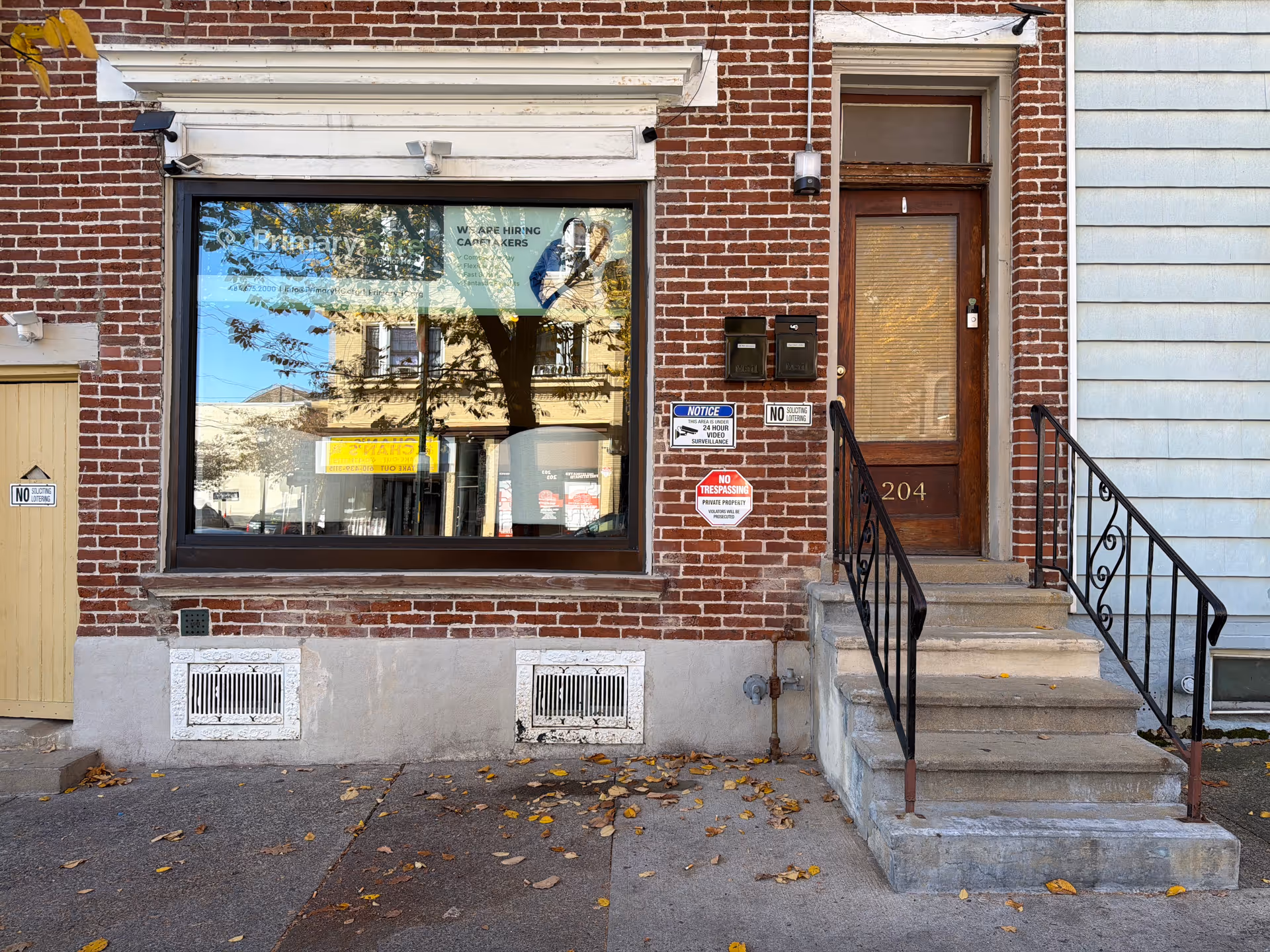 Brick building with a large storefront window and a wooden entry door, stairs on the right.