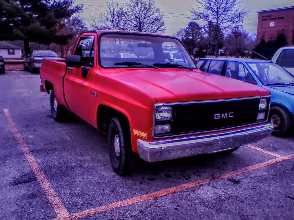 Red GMC pickup truck parked in a lot with other vehicles.